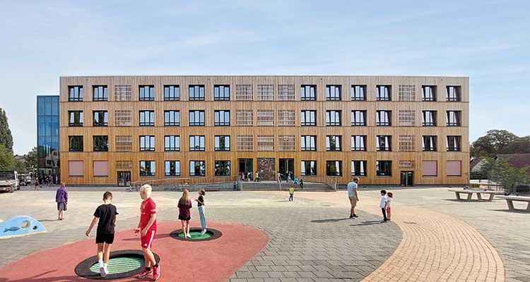 Das Bild zeigt die Front des sanierten Hauptgebäudes der Wilhelm-Gentz-Grundschule mit einer Fassade aus Lärchenholz. 