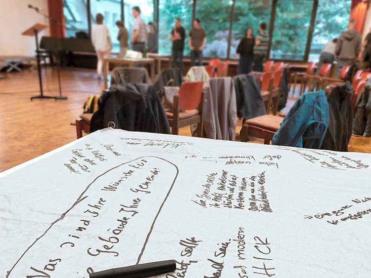 Workshopraum mit einem liegenden beschriebenen Whiteboard im Vordergrund und Stühlen und Teilnehmern im Hintergrund 