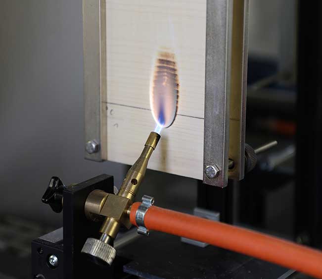 Das Bild zeigt den Einzelflammentest nach EN-ISO 11925-2 für die flammschützende Wirkung der neuen Holzbeschichtung im Brandlabor des Fraunhofer WKI am Beispiel von Fichtensperrholz. 