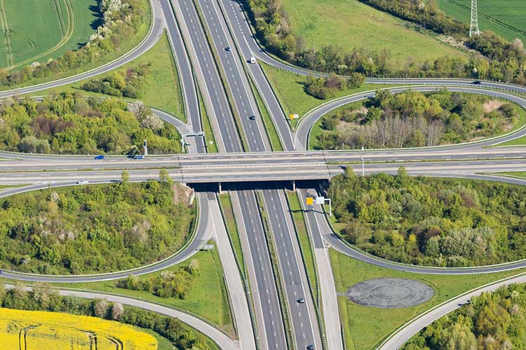 Luftaufnahme einer Autobahnbrücke mit den Ausfahrten von und den Auffahrten auf die Autobahn in einer stark begrünten Umgebung. 