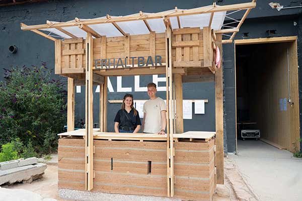Das Bild zeigt die Architektur-Studierenden Carla Lorenzen und Tarek Hansen in der aus Stampflehm errichteten »erhaltbar« auf dem Schlachthofgelände