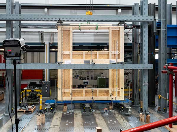 Eine zweigeschossige Hauswand mit Fensteröffnungen wird im Prüfstand kontrolliert unter Druck gesetzt.