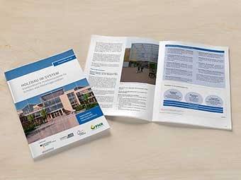 Auf einem hellen Untergrund liegen zwei Exemplare der Broschüre »Holzbau im System«. Links ist das Cover zu sehen, das Exemplar rechts daneben ist aufgeklappt. 